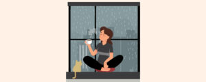 A person drinking coffee near the window beside her pet cat